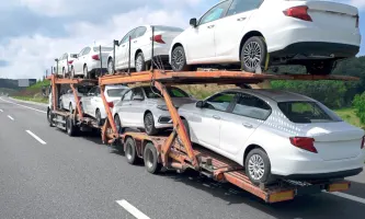 A double-decker stinger car hauler carries a full load of new white vehicles along an interstate highway.