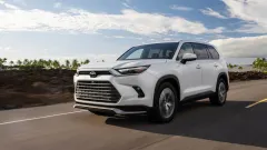 White 2027 Toyota Grand Highlander Limited driving on a paved road with palm trees and blue sky in the background.