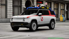 White Rivian R1S SUV customized as the Ghostbusters Ecto-R1, featuring the Ghostbusters logo, red accents, roof-mounted equipment, and emergency-style lights.