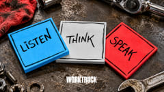 Three overlapping sticky notes in Work Truck brand colors reading “Listen,” “Think,” and “Speak” sit on a worn automotive workbench surrounded by tools and hardware.