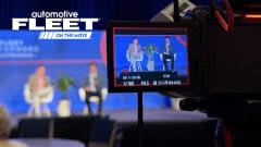 A camera monitor shot of two people on a conference stage. 