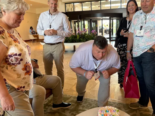 A man blows out a birthday cake with onlookers.