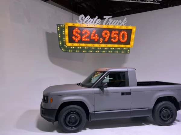 Slate pickup truck in front of a neon lit price-tag sign