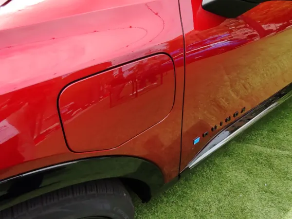 Close up photo of side of red car showing the door that opens to access the charging port.