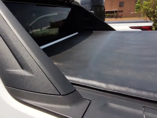 Close-up view of black tonneau cover on white pickup truck.