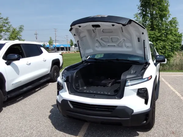 Front view of a white EV pickup truck with the hood, or front e-trunk, open.