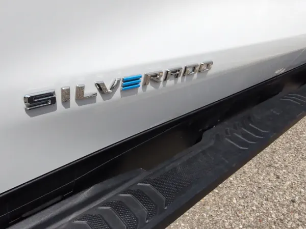 Close up photo of the side of a white truck with the word Silverado in chrome, the E is in blue to signify it as an electric vehicle.