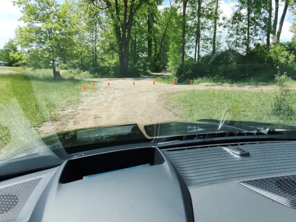 View from driver's position looking out the windshield and over the hood of a black pickup truck driving on a dirt path.