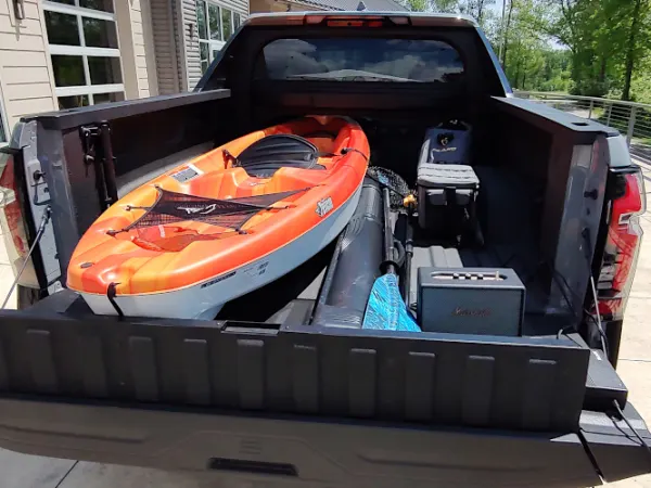 An orange kayak and other gear is loaded in the bed of a black pickup truck.