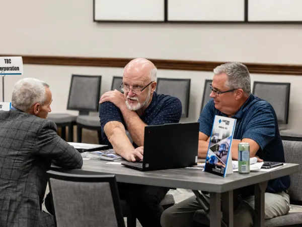 Three attendees at a table talking with marketing materials and laptops at Work Truck Exchange.