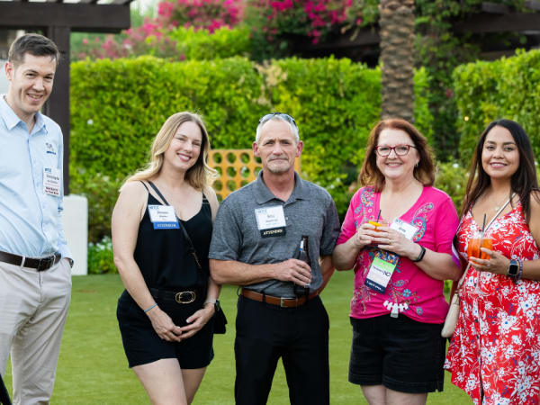 Group of Work Truck Exchange 2025 attendees smiling and posing together at the outdoor evening networking reception under palm trees.