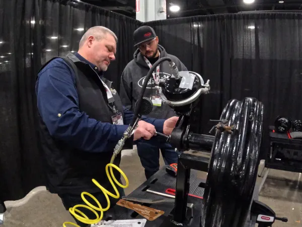 Two men talking about a large automotive part on a stand.