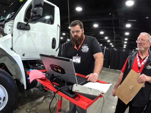 Technician working on laptop with a truck in the background.