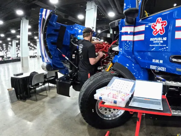 Repair technician, shown from behind, working under the hood of a large truck.