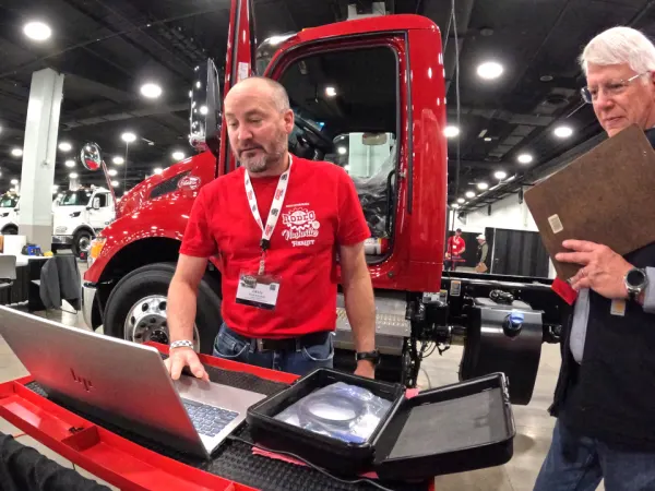 Technician working on laptop with a truck in the background.