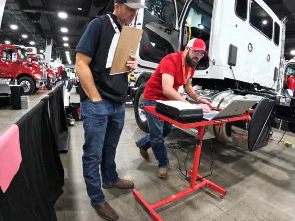 Technician working on laptop with a truck in the background.
