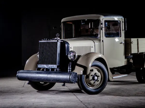 Beige 1937 Mercedes-Benz L 1500 truck with wood-gas generator displayed indoors, illustrating early alternative fuel technology.