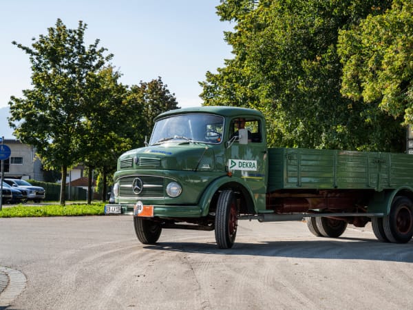 Restored green vintage Mercedes-Benz flatbed truck driving on a tree-lined street, representing post-war commercial transport history.