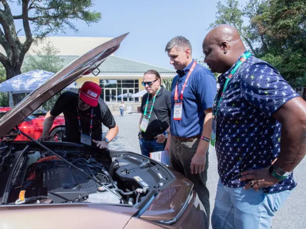 Four men peer under hood of car. 