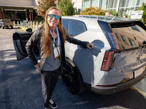 A man poses with sunglasses on next to an SUV. 