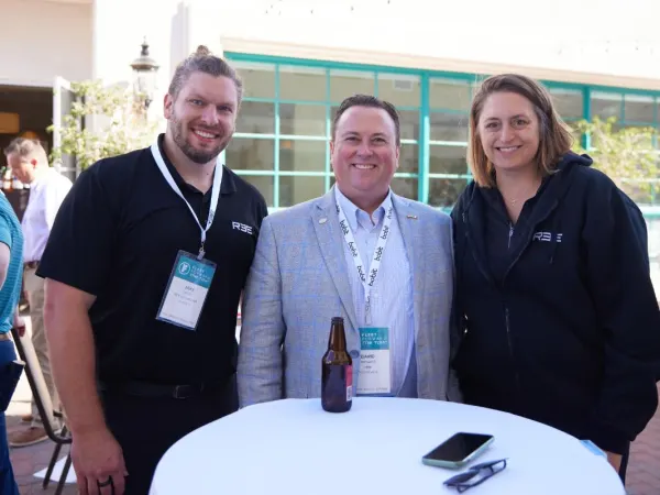 Three event attendees pose at a cocktail table. 