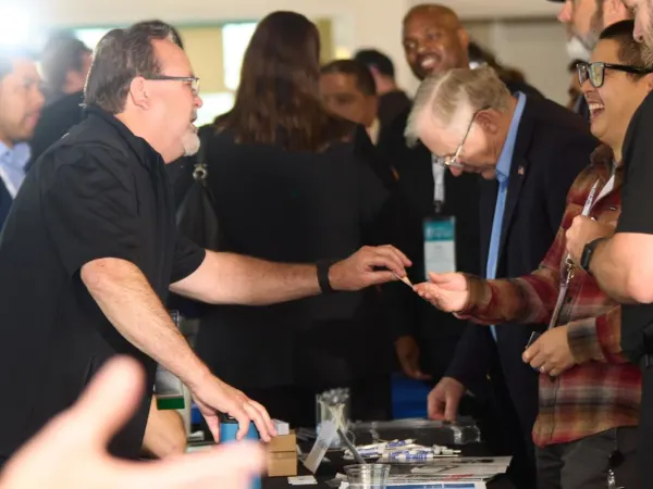 A man hands a business card to an attendee across a table. 