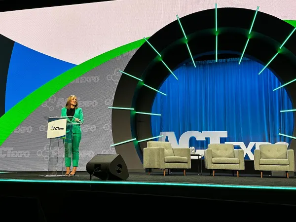 A woman on stage addresses the audience. 