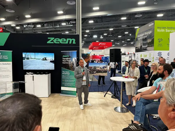 Man with microphone speaks to reporters at trade show booth. 