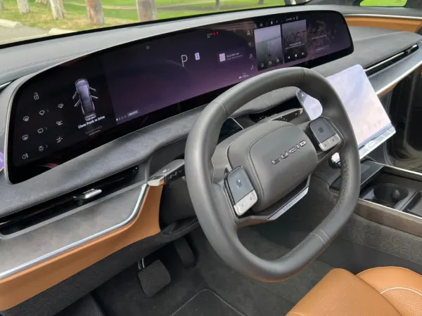 Left driver side view of steering wheel and long dark electronic dashboard screen.