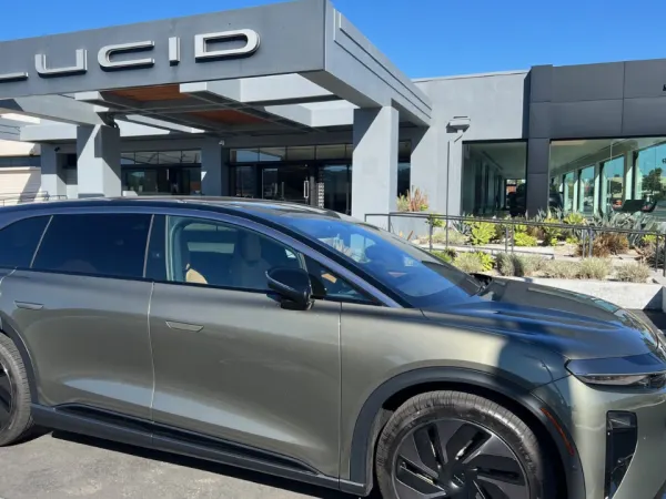 Right-side view of a gray Lucid Gravity in front of a Lucid dealership, with a porte cochere facing forward bearing the Lucid logo.