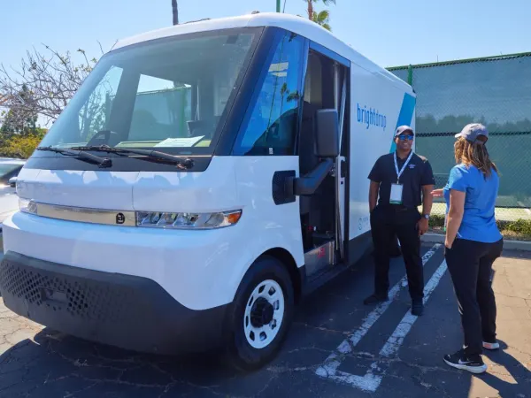 Two people talk next to an electric van. 