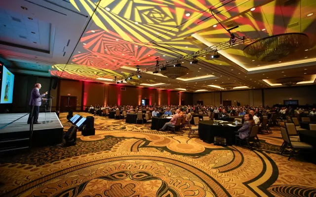 Wide shot of main ballroom with attendees sitting. 