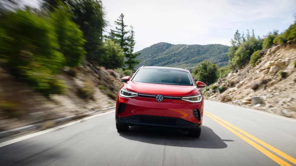 A red Volkswagen ID.4 is seen driving down a winding, mountainous road.