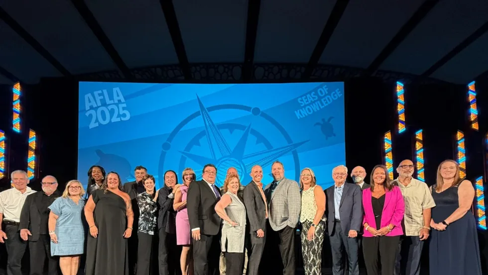 A group of AFLA award winners stand on a stage in front of a blue background with AFLA on the front.