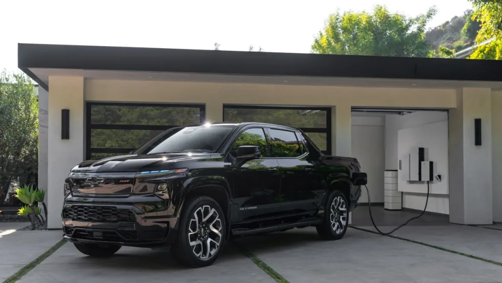 Pickup truck sits outside luxury home's garage getting charged.