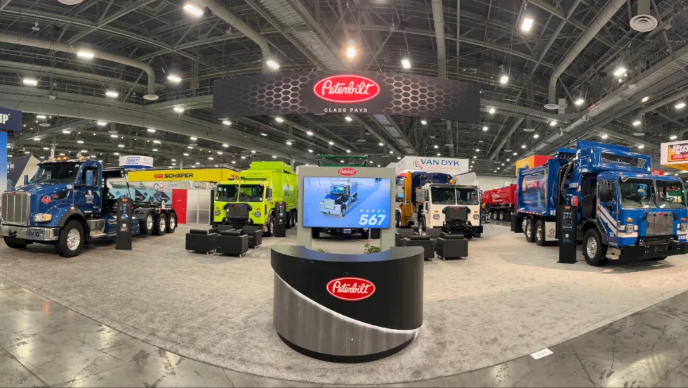 Four Peterbilt refuse trucks are parked in an exhibit space at WasteExpo.