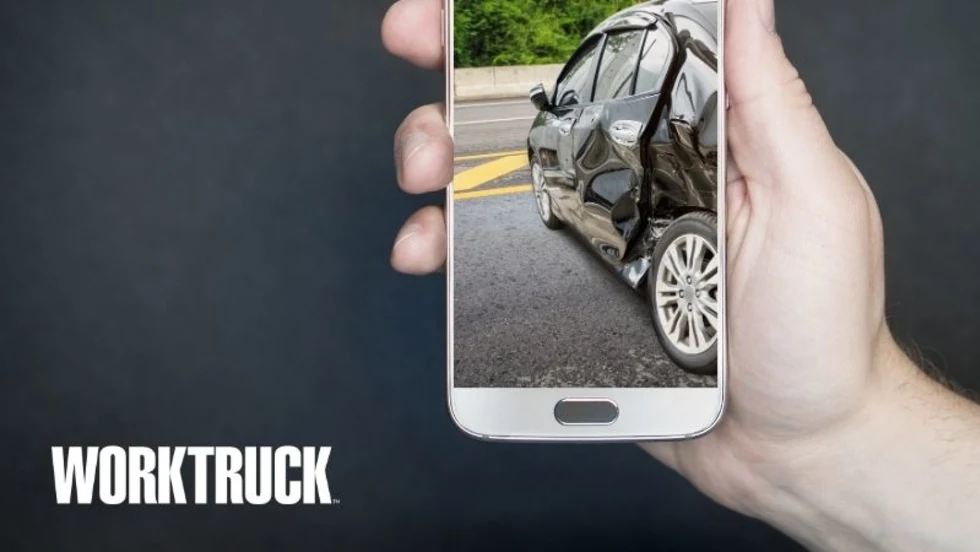 Person holding a cellphone with an image on the screen of a car that has been involved in a collision.