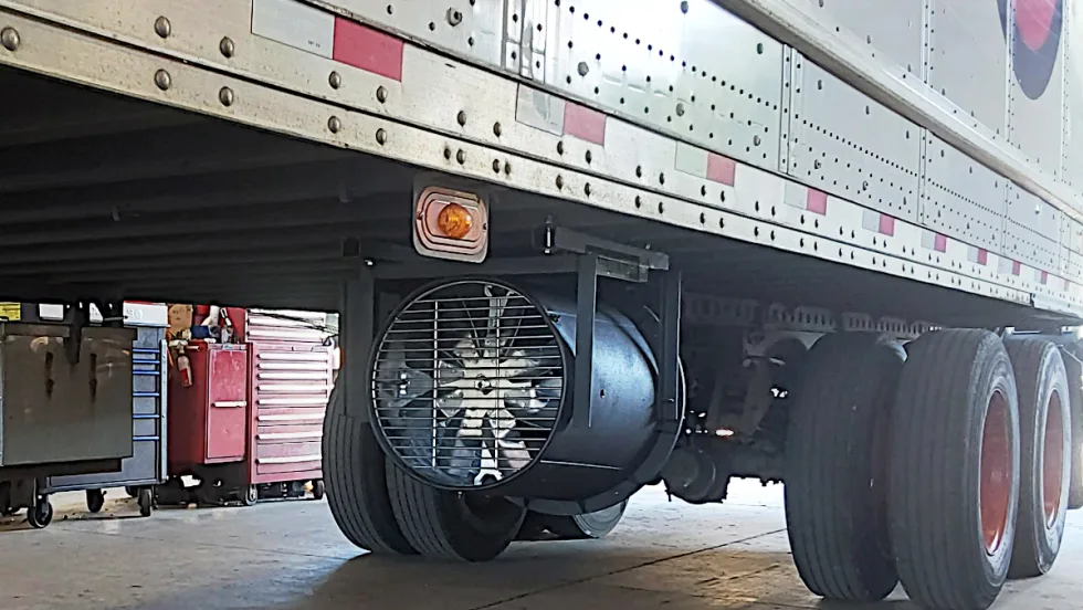 A cylindrical metal tube with fan blades is installed beneath a trailer.