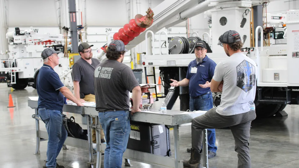 Men standing around a table in a warehouse, engaged in a discussion.
