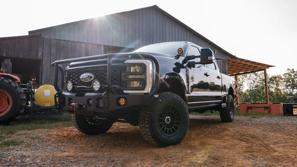 Angled view of a lifted black pickup truck parked in front of a barn.