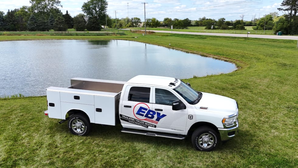 White truck with service body parked by a lake with Eby logo on side in blue.