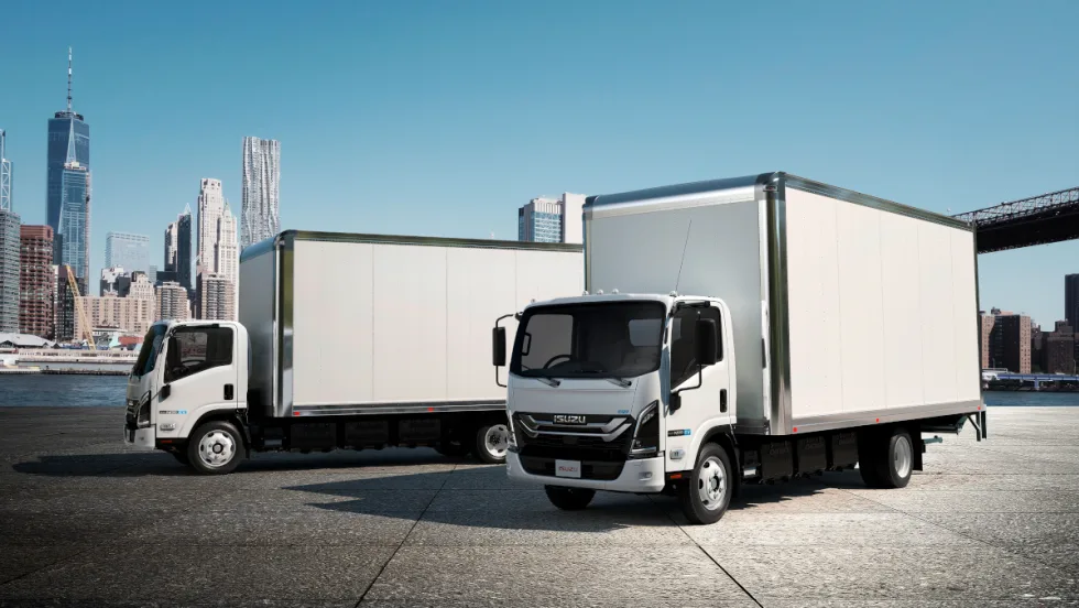 Two white box trucks parked in front of a city skyline.