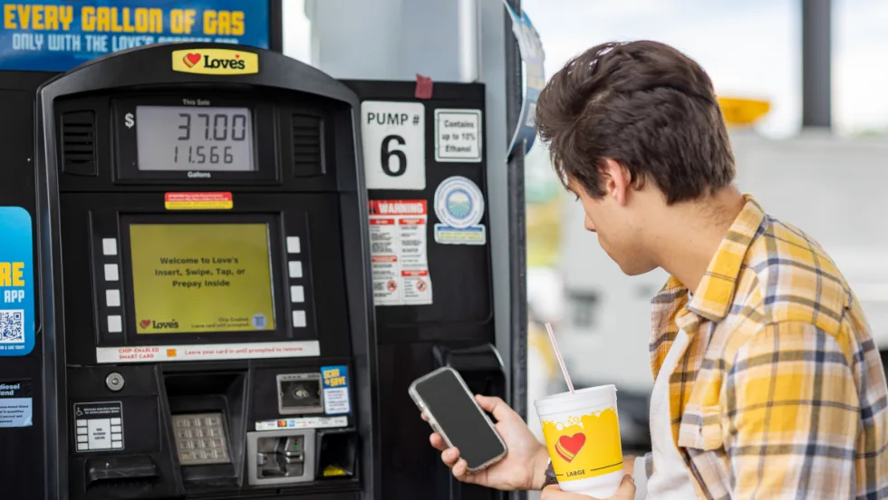 Young man looks at a fuel discount app while at a fuel pump.
