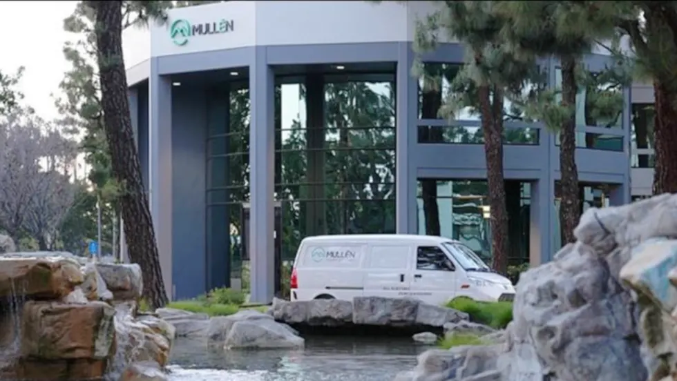 White cargo van parked in front of a landscaped corporate building with Mullen logo.