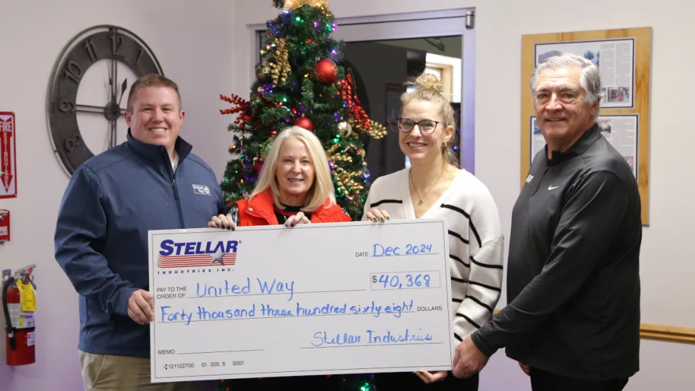 Four business people hold a large symbolic check as part of a charitable donation.