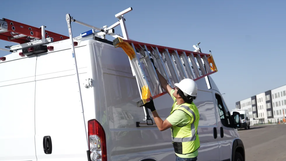 Man unloads ladder of the rack of a work van.