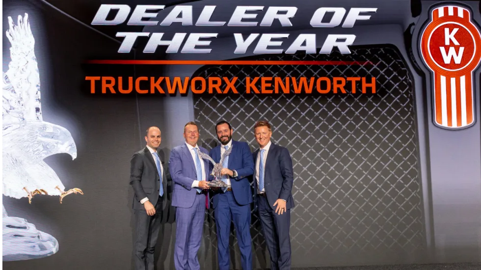 Men in business attire on a stage presenting and receiving an award.