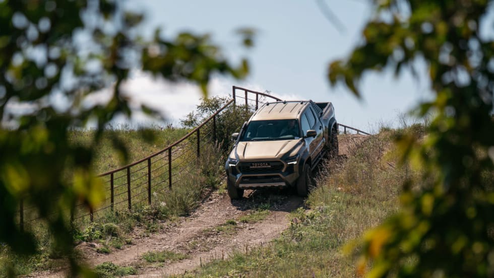 View through trees of a pickup truck cresting a hill in a farm setting.