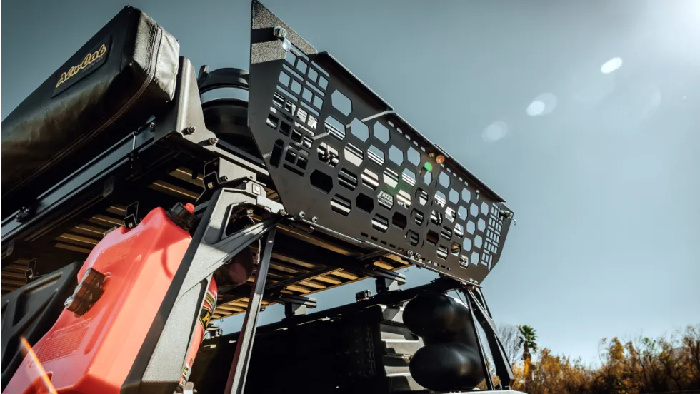 metal gate locks the area above the tailgate of a pickup truck. Photo shows it open against a blue sky.