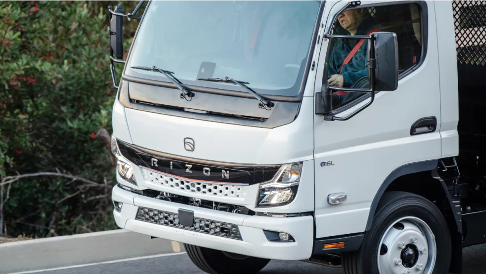 close-up photo of a man driving a white battery electric truck.
